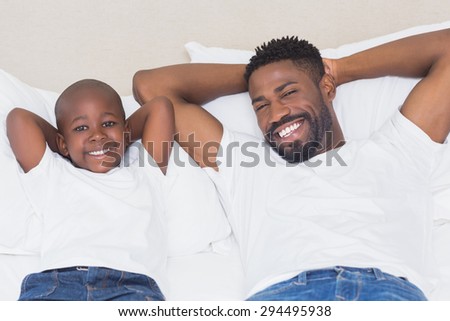 Father and son smiling at camera at home in bedroom