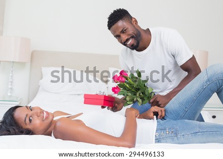 Romantic man giving roses to partner at home in bedroom