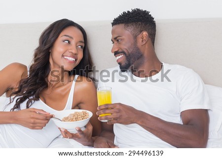 Relaxed couple in bed together eating cereal at home in bedroom