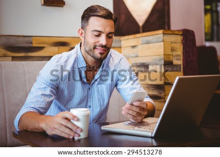 Smiling businessman sending a text message with laptop beside at the cafe