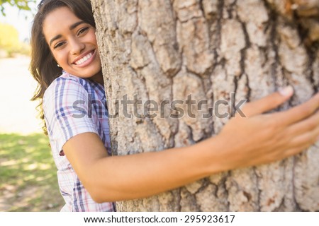 Pretty brunette hugging tree on a sunny day