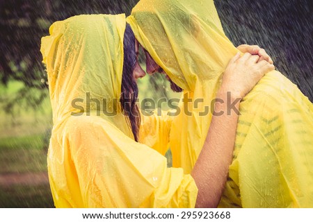 Cute couple wearing protection cape and hugging under the rain in the park