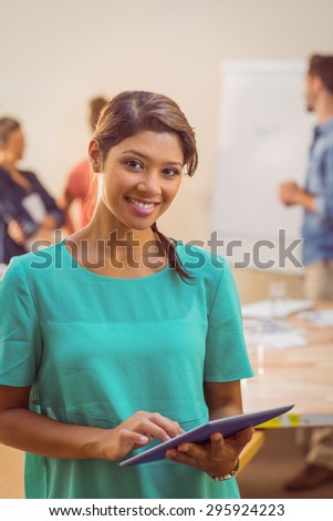 Casual businesswoman using tablet and looking at camera during a meeting