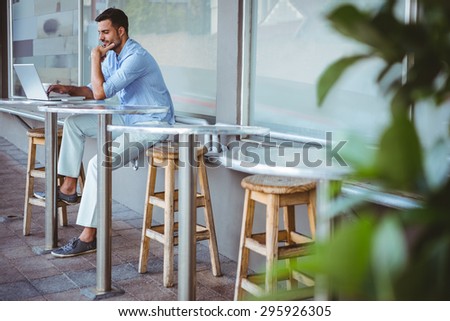 Distant view of a thoughtful businessman using his laptop outside the cafe