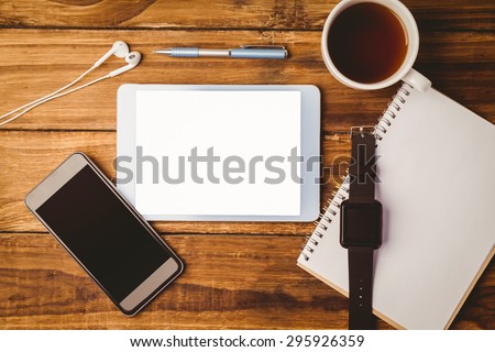 `Tablet ans smartphone and swatch on notepad next to cup of coffee on wooden table