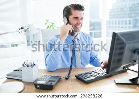 Smiling businessman using his computer and phoning on his office