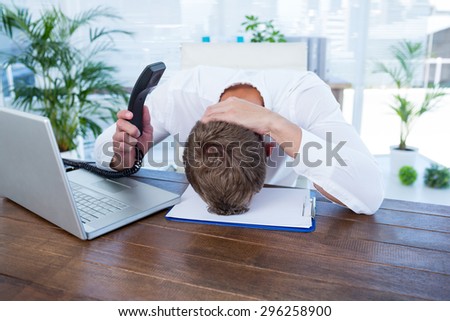 Irritated businessman holding a land line phone in the office