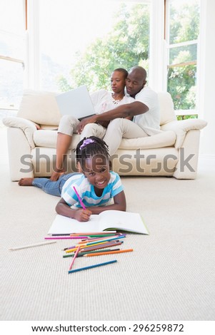 Pretty couple using laptop on couch and their daughter drawing in living room