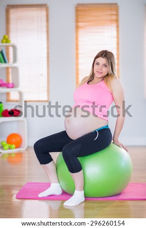 Pregnant woman looking at camera sitting on exercise ball in the living room
