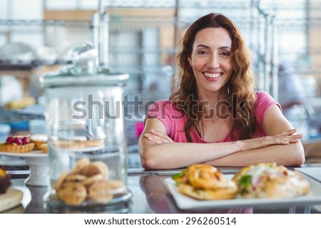 Pretty brunette smiling at camera behind counter at the bakery