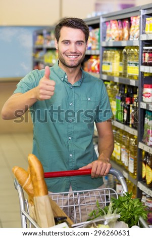 Portrait of smiling man buy products with his trolley and thumb up at supermarket