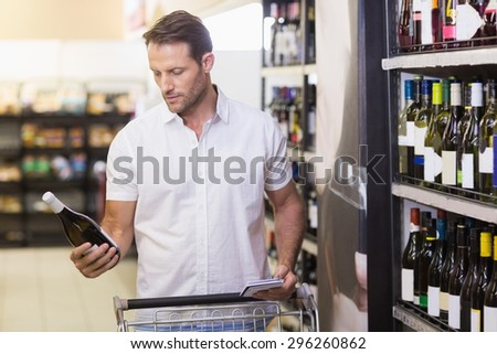Handsome looking at a wine bottle having in her hands in supermarket