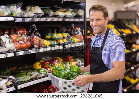 Portrait of a smiling handsome worker holding a box with vegetables in supermarket