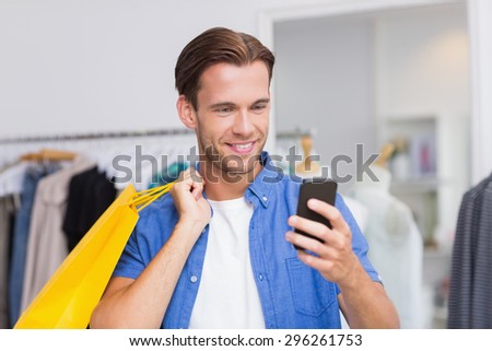 A smiling man with shopping bags looking at his smartphone at the clothing store