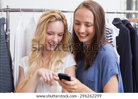 Smiling friends looking a smartphone in a boutiaue