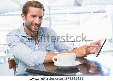 Young happy man smiling at the camera and pointing at the phone in the cafe