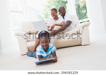 Pretty couple using laptop on couch and their daughter using tablet in living room