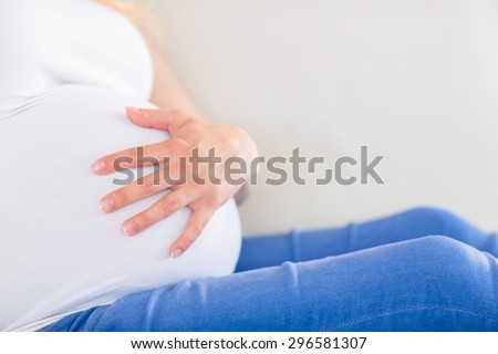 Close up of pregnant woman with one hand on belly lying on the couch