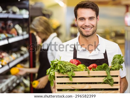 Portrait of a smiling staff man holding a box of fresh vegetables at supermarket