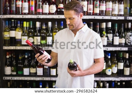 A handsome looking at wine bottle in supermarket