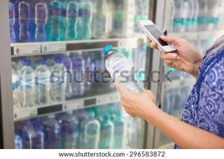 Woman comparing the price of a bottle of water with her phone at the supermarket