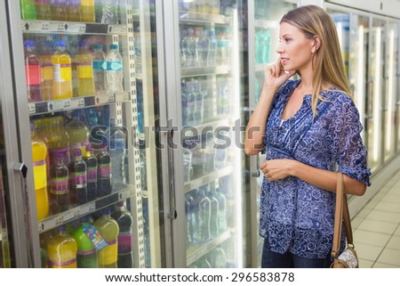 Portrait of a pretty smiling blonde woman buying frozen products and phoning at supermarket