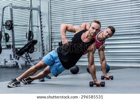 Muscular men doing a side plank while lifting a dumbbell