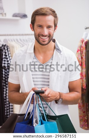 Portrait of smiling man with shopping bags using smartphone at a boutique