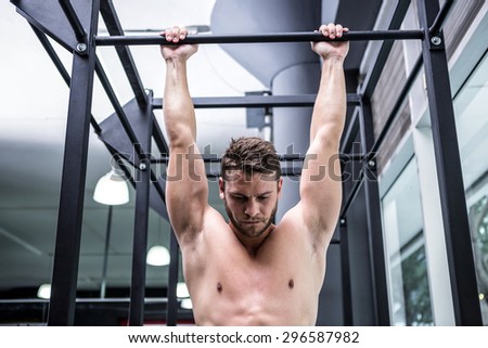 Muscular man doing pull ups in crossfit gym