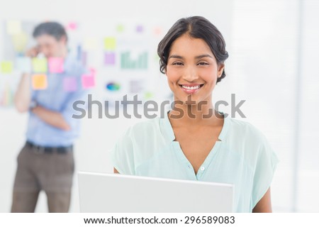 Businesswoman presenting laptop screen with colleague behind her in the office