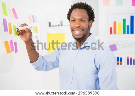 Young smiling businessman writing on sticky notes in the office facing towards the camera