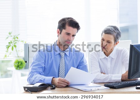 Two business people looking at a paper while working on computer in the office