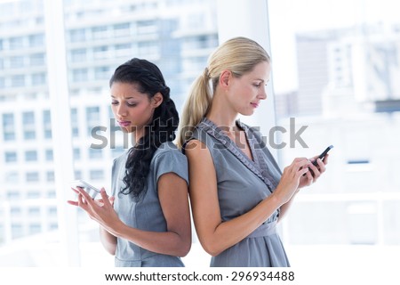 Back to back businesswomen texting messages in the office