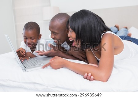 Pretty family using laptop together in bed at home in bedroom