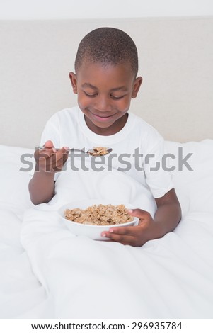 Pretty little boy eating cereals in bed at home in bedroom