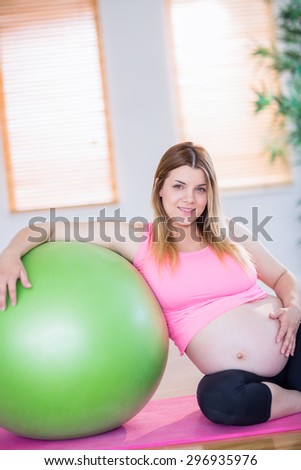 Pregnant woman looking at camera next to exercise ball in the living room