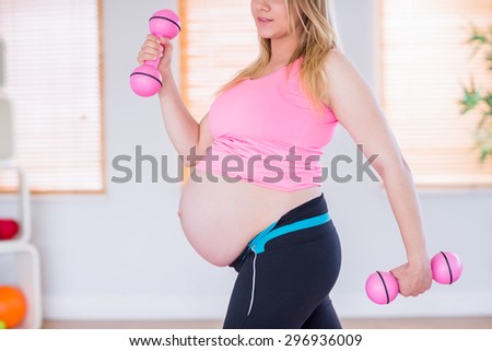 A pregnant woman holding dumbbells at home