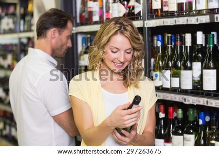 Smiling pretty blonde woman looking at wine bottle in supermarket