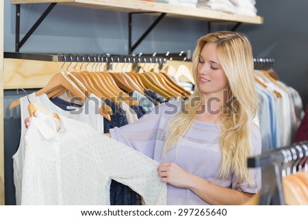 Pretty blonde woman choosing clothes in clothes store