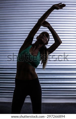 Front view of a muscular woman stretching in shadow room