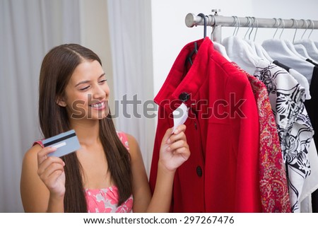 Smiling woman looking at red coat and holding credit card at a boutique