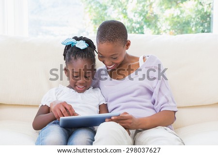 Happy smiling mother using tablet with her daughter on couch in living room
