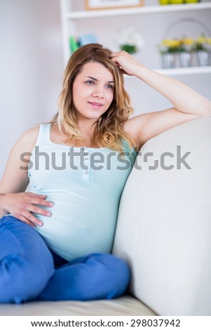 Pregnant woman looking away with hand in hair at home in the living room