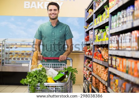 Portrait of smiling man walking with his trolley on aisle at supermarket