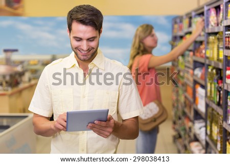 Smiling handsome man using a digital tablet at supermarket