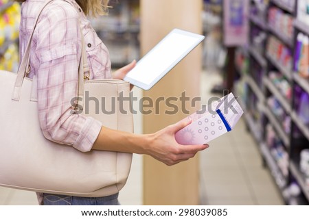 Pretty blonde woman looking at a product and using her digital tablet in supermarket