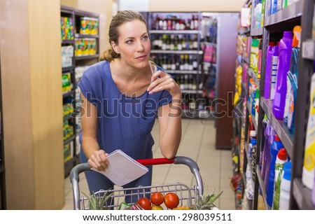 Pretty woman looking at product on shelf and holding grocery list at supermarket