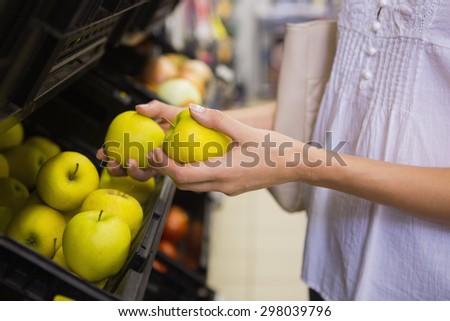 Smiling pretty blonde woman buying apples at supermarket