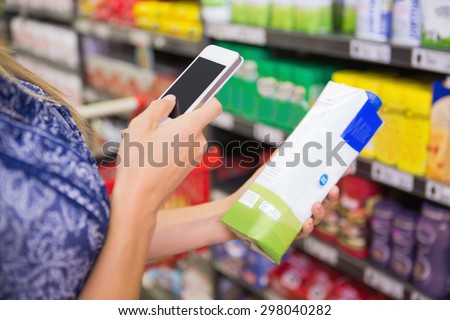 Woman comparing the price of a carton of with her phone at the supermarket