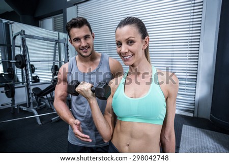 Portrait of a muscular woman lifting dumbbells helped by a coach